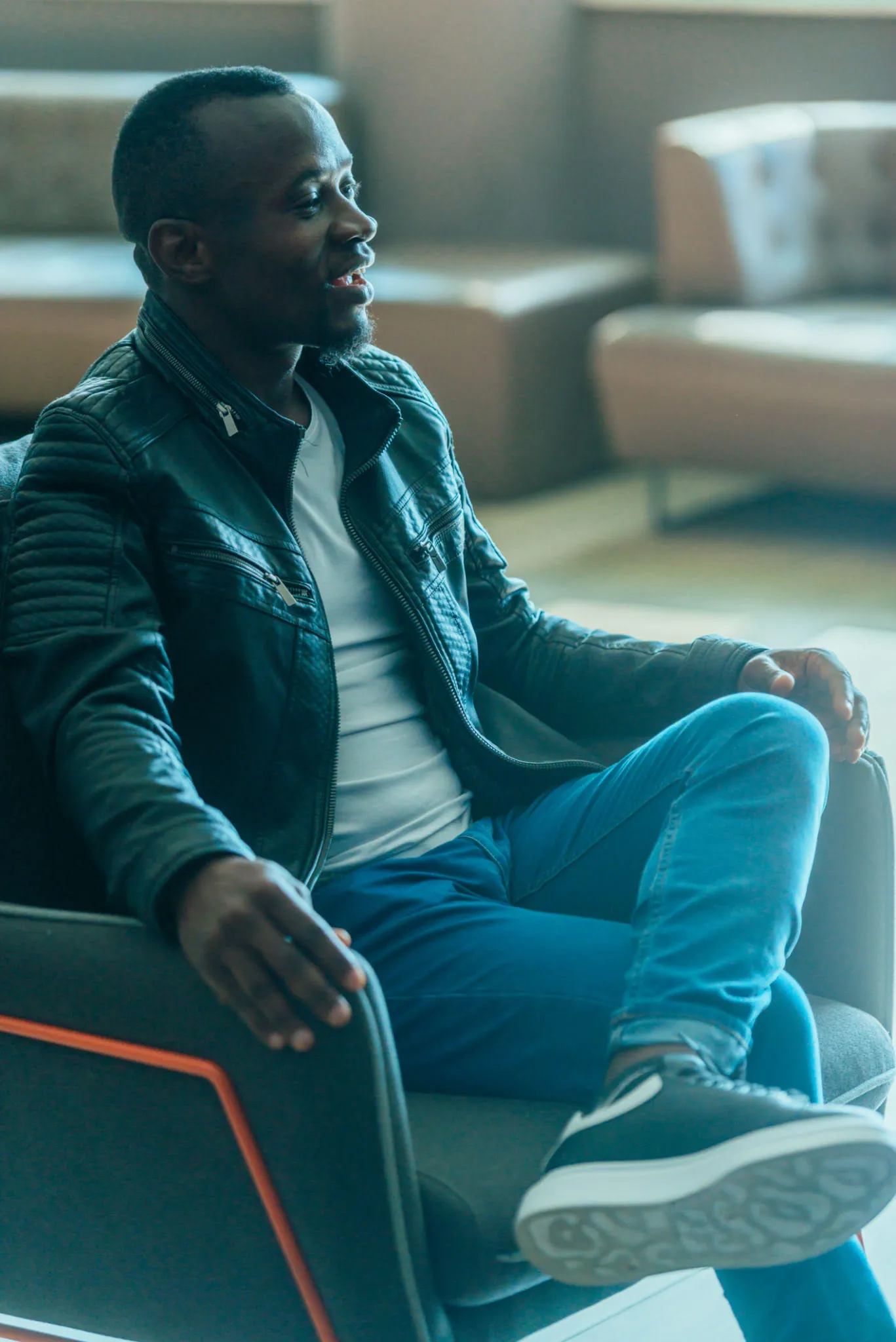 A man sits back in a lounge chair, mid-conversation, at ease.
