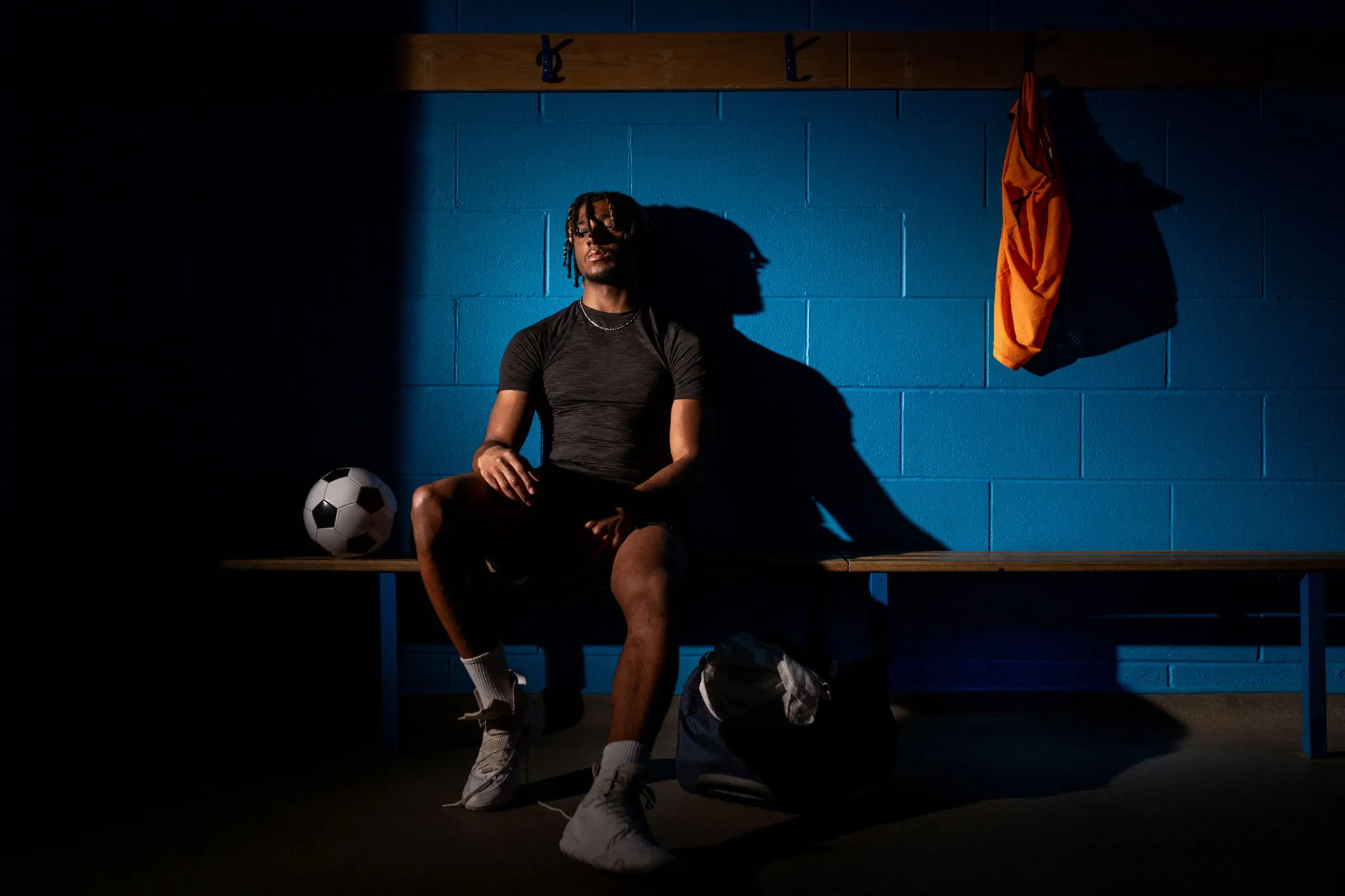 A young athlete sits alone on a locker-room bench under a shaft of light.